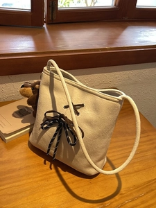 Elegant beige suede bucket bag with stylish bow tie detail on a natural wood surface