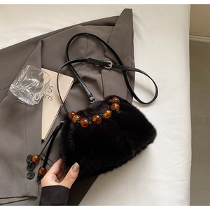 Close-up of black faux fur crossbody bag with amber bead detail on a grey suit