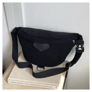 Detail of black corduroy chest bag featuring textured fabric and leather patch on art book