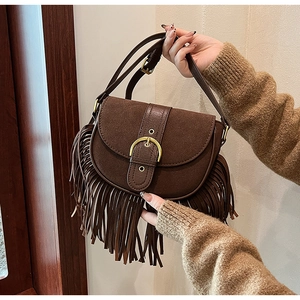Detailed close-up of dark brown suede saddle bag featuring long tassels and gold buckle