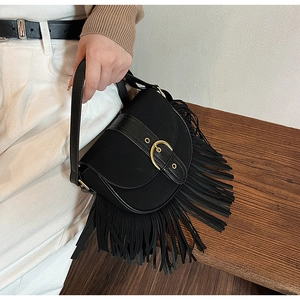 Detail of vintage black suede saddle bag with golden buckle and stylish long tassels