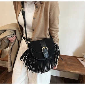 Detailed view of a black tassel saddle bag worn by a model against a minimalist wall