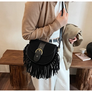 Detail of a black suede saddle bag featuring long fringe tassels and golden buckle