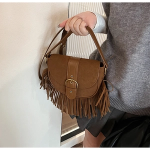 Detail view of brown vintage saddle bag featuring fringe tassels and gold buckle closure