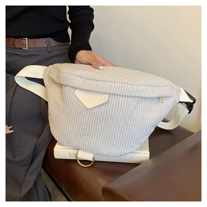 Close-up of white corduroy waist bag with metal ring and soft texture on leather bench