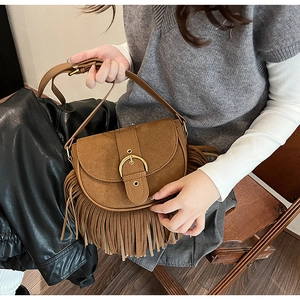 Detail of vintage brown suede saddle bag with long tassels and gold metal buckle
