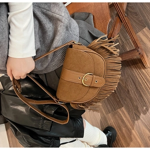 Detail of vintage brown suede saddle bag featuring long fringe tassels and metal buckle