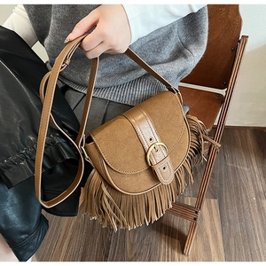 Close-up of brown vintage fringe saddle bag with matte texture and gold buckle detail
