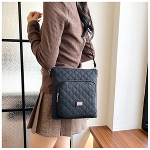 Close-up of black quilted nylon crossbody bag with metal plate detail on a model