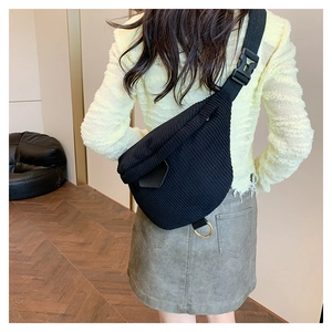Detail view of black corduroy chest bag featuring an adjustable strap and gold metal ring
