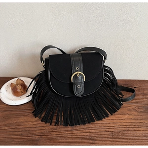 Detail of vintage black tassel saddle bag with gold buckle on wooden background