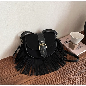 Detail of black matte saddle bag with fringe tassels and gold buckle on a wooden surface