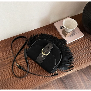 Close-up of bohemian black suede saddle bag with long fringe and gold buckle on wood