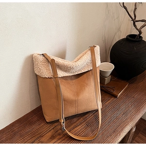 Dettaglio borsa a secchiello in camoscio marrone con bordo in montone beige su tavolo in legno