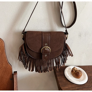 Close-up of vintage brown suede saddle bag with tassel details and a gold metal buckle
