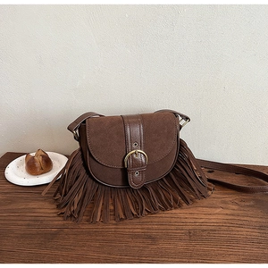 Detailed macro view of dark brown tassel saddle bag with vintage buckle and suede texture