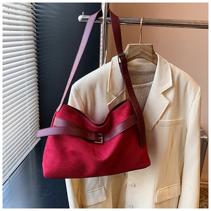 Détail d'un sac cabas en daim rouge avec lanière en cuir sur un blazer beige