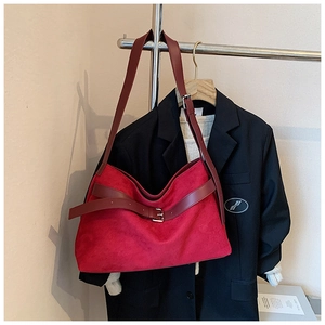 Détail d'un grand sac cabas rouge en daim avec boucle en métal à côté d'un costume noir