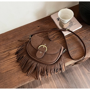 Detailed close-up of brown fringe saddle bag on a wooden bench with rustic aesthetic