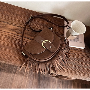 Detail of a brown fringe saddle bag on a wooden table with vintage hardware and texture
