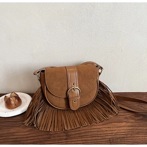 Close-up of brown vintage saddle bag featuring fringe tassels and bronze buckle on wood