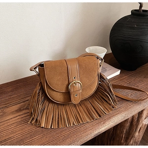 Detail of vintage brown saddle bag with long tassels and metallic buckle on wood