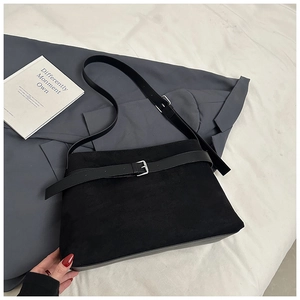 Détail du sac à bandoulière noir mat avec œillet argenté sur un costume gris