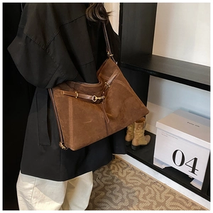 Detail of a large brown suede tote bag featuring artistic straps and golden hardware buckles