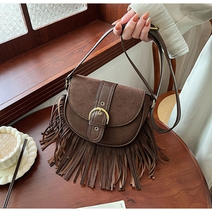 Detail view of brown frosted saddle bag featuring retro tassels and a metal buckle on wood