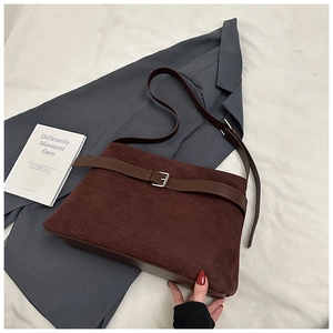 Détail d'un sac cabas en daim marron foncé avec boucle argentée sur une literie neutre