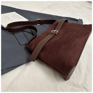 Détail d'un sac bandoulière en daim marron foncé avec boucle en cuir et bandoulière réglable