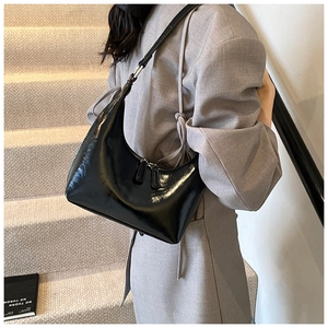 Dettaglio della borsa Hobo minimalista in pelle verniciata nera su abito grigio