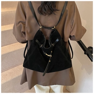 Back view of a model wearing a large black matte suede hobo backpack with gold hardware