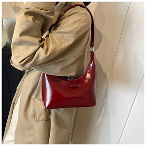 Dettaglio della borsa sottobraccio in pelle lucida rosso scuro con trench color kaki