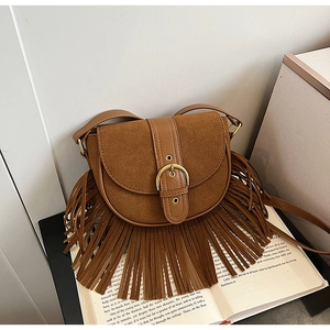Detail view of vintage brown saddle bag with long tassels and metallic buckle on books