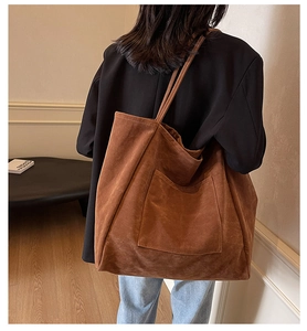 Detail view of large brown suede tote bag with front pocket carried by a model