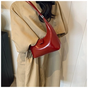 Dettaglio di una borsa a mezzaluna in pelle bordeaux abbinata a un trench chic
