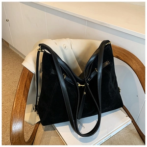 Close-up of black suede tote bag with leather straps and gold hardware on a wooden chair