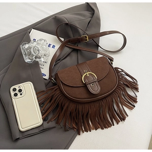 Close-up of vintage brown suede saddle bag featuring a large bronze buckle and long tassels