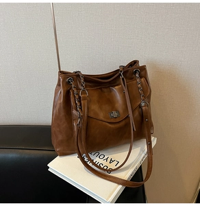 Dettaglio borsa tote in pelle marrone con tracolla a catena e chiusura a scatto in metallo