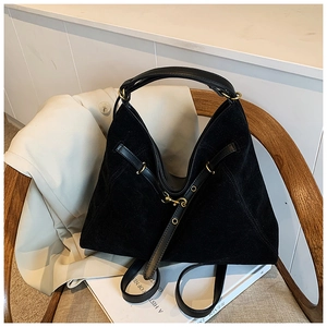 Detail of a black suede tote bag with gold hardware placed on a wooden chair