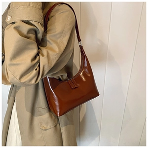 Dettaglio della borsa hobo in pelle marrone lucida indossata da una modella in trench