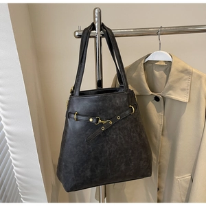 Detailed close-up of a vintage black leather tote bag with elegant gold metal ring buckle