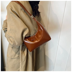 Dettaglio della borsa hobo marrone lucida indossata con un trench kaki alla moda