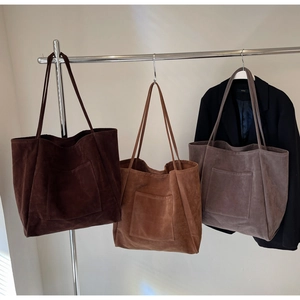 Close-up of three suede tote bags in dark brown, caramel, and taupe with stitching details
