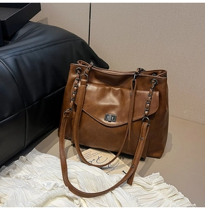 Dettaglio di una borsa tote marrone con tasca a girello in metallo e tracolla a catena