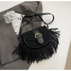 Detail of black crossbody saddle bag featuring suede tassels and a gold buckle on a blazer