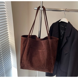 Close-up of a brown suede tote bag with front pocket detail hanging on a metal rack