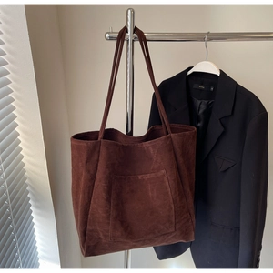 Detail of large dark brown suede tote bag featuring a front pocket and soft matte texture