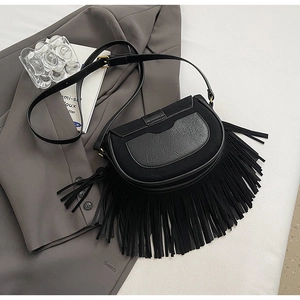 Detail of a black tassel saddle bag featuring matte fabric and pebble leather texture